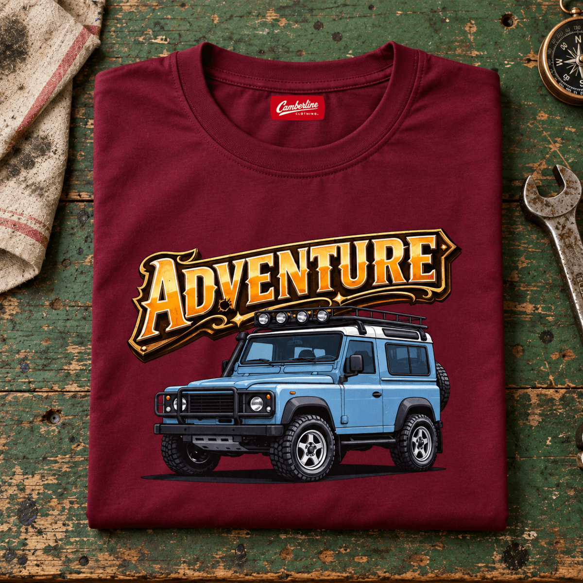 Folded burgundy adventure off road 4x4 T-shirt, front print on a worn workshop bench — car-ts-0002