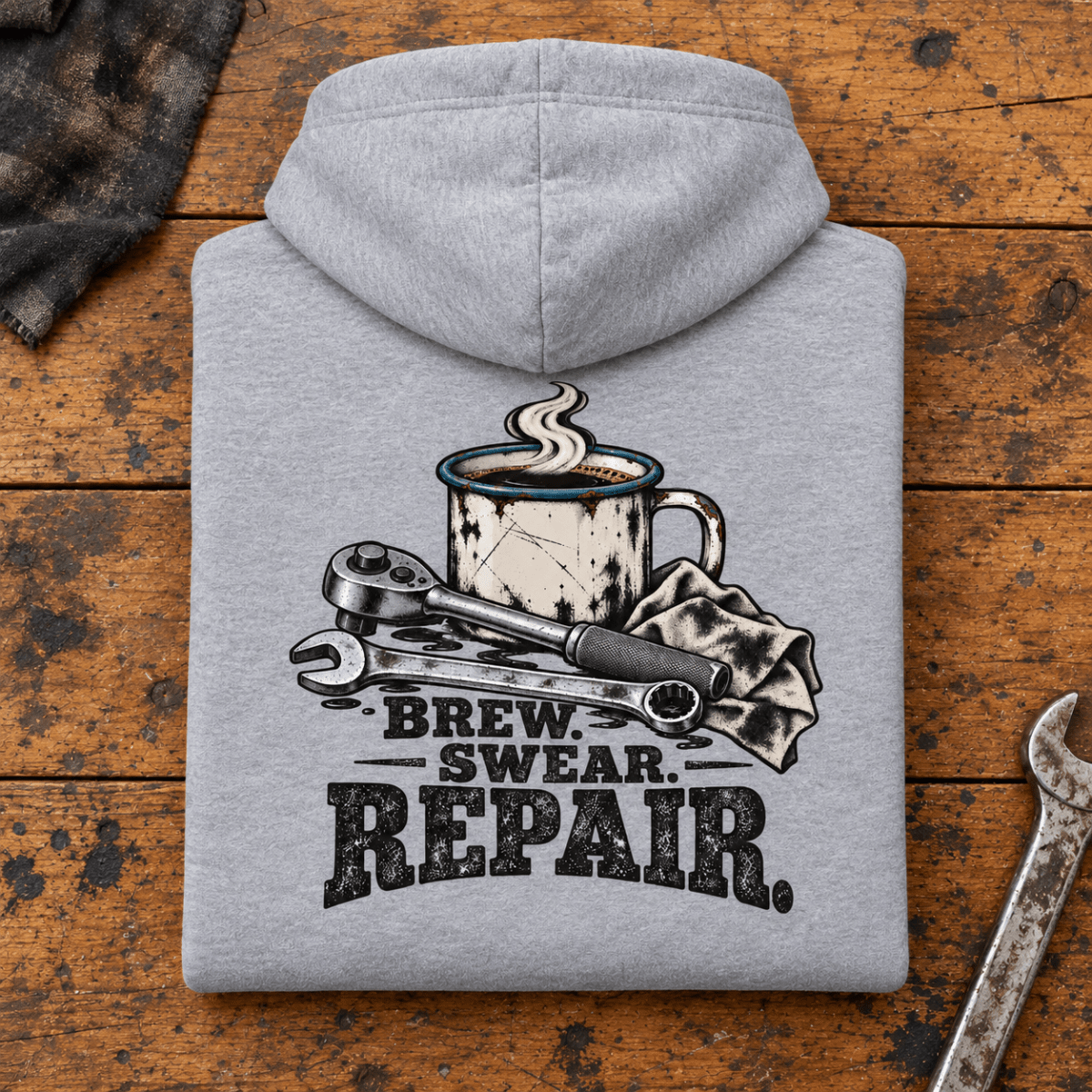 Camberline Coffee and Tools Mechanic Hoodie in heather grey, folded back view on a workshop bench with full graphic visible