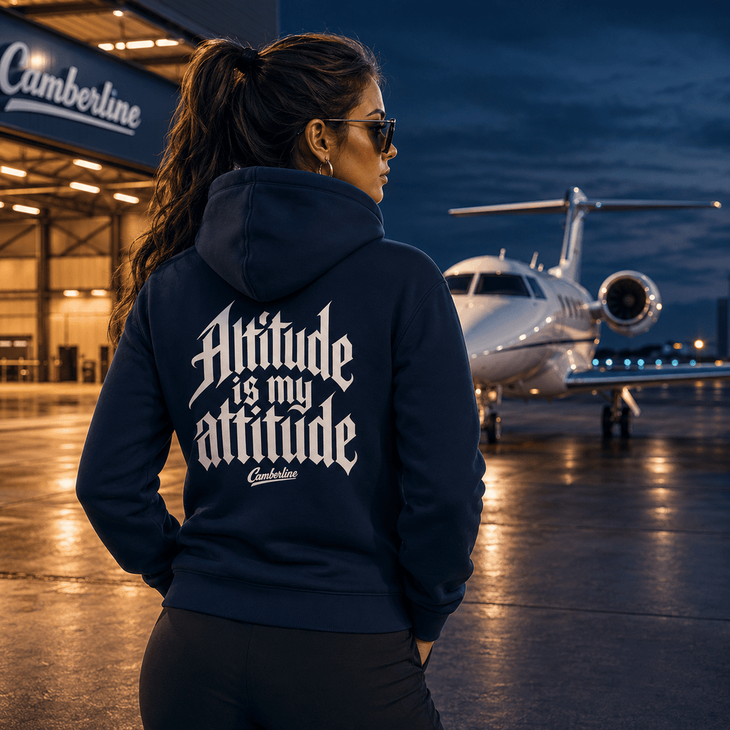 Person wearing a hoodie with 'Altitude is my attitude' text in front of an airplane at an airport.