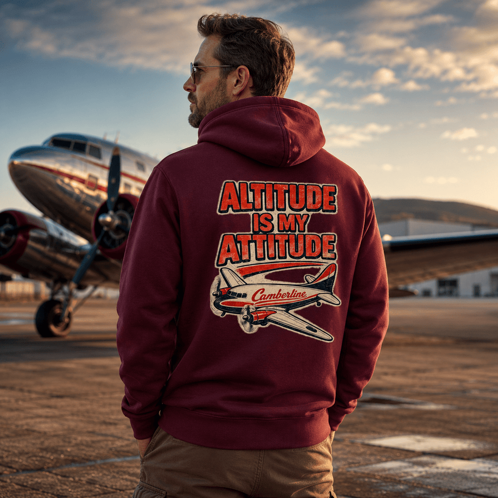 Man wearing a hoodie with 'Altitude is My Attitude' text and airplane graphic, standing in front of an airplane on a runway.