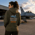 Person wearing a hoodie with 'Fighting Falcon' design in front of a fighter jet on an airfield.
