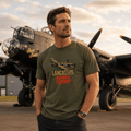 Man wearing a green t-shirt with an airplane design in front of a vintage airplane.
