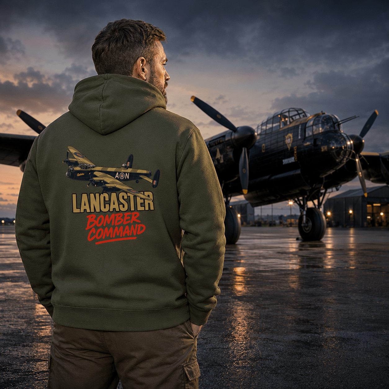 Person wearing a green hoodie with 'Lancaster Bomber Command' text and airplane design, standing in front of a vintage airplane on an airfield.