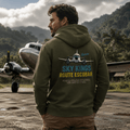 Man wearing a hoodie with 'Sky Kings Route Escobar' design, standing on an airstrip with an airplane in the background.