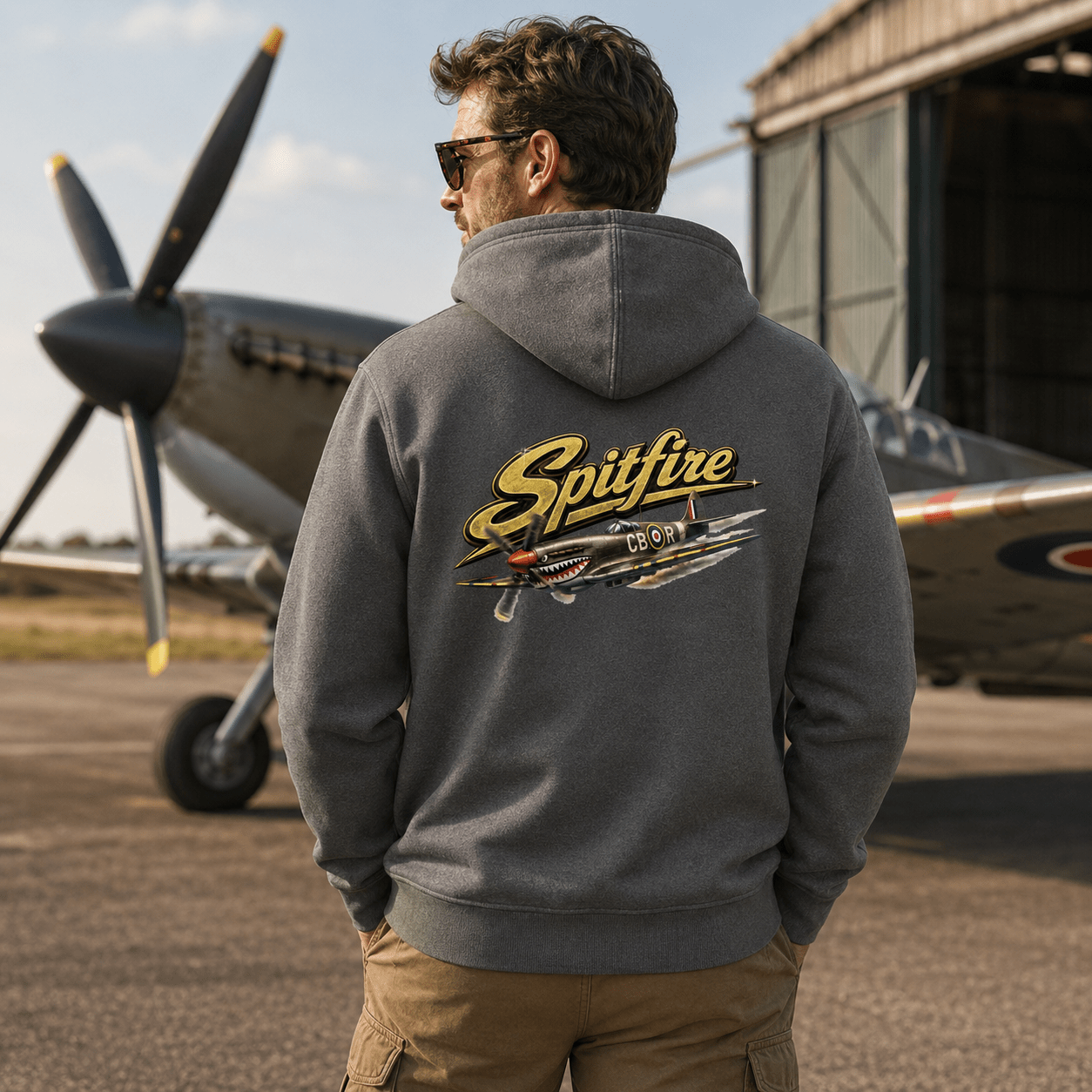 Person wearing a hoodie with 'Spitfire' design in front of a vintage airplane.