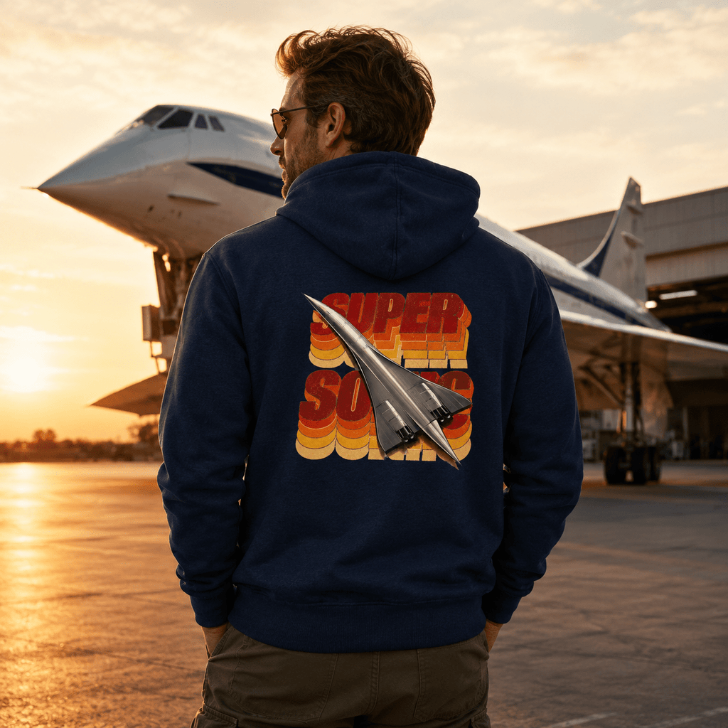 Person wearing a hoodie with a retro airplane design in front of an airplane at sunset.