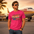 Man wearing a pink t-shirt with an airplane graphic and text, standing in front of an airplane at an airport.