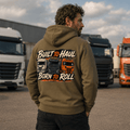 Man wearing a hoodie with 'Built to Haul, Born to Roll' text and truck graphics in front of trucks.