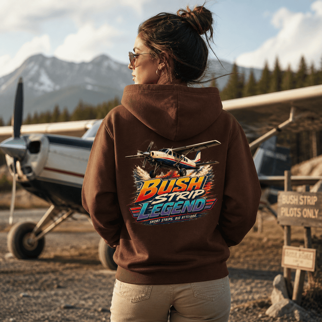 Person wearing a hoodie with 'Bush Strip Legend' design in front of a small airplane and mountains.