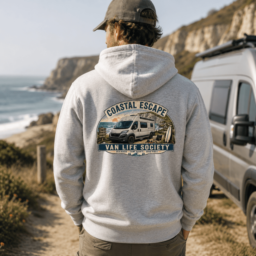 Person wearing a hoodie with 'Coastal Escape Van Life Society' design, standing near a van by the coast.