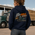 Person wearing a hoodie with 'Eat. Sleep. Haul. Repeat.' text and truck graphic, standing in front of a truck.