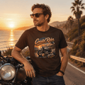 Model wearing the Camberline Riders Coastal Rider Motorcycle T-Shirt – Hot Chocolate, showing the Riders front graphic in a motorcycle-inspired setting