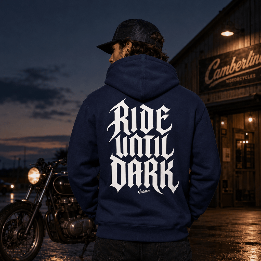 Model wearing the Camberline Riders Ride Until Dark Gothic Typography Hoodie – Navy, showing the Riders back graphic in a motorcycle-inspired setting