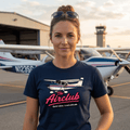 Woman wearing a t-shirt with an airplane graphic and text, standing in front of airplanes at an airport.