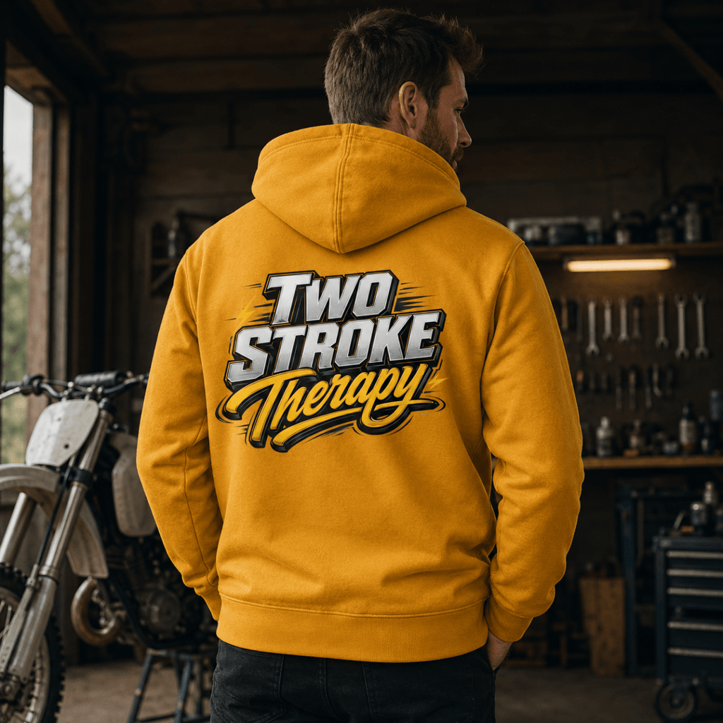 Camberline Two Stroke Therapy motorcycle hoodie in mustard yellow, worn by male model in workshop garage setting, back view