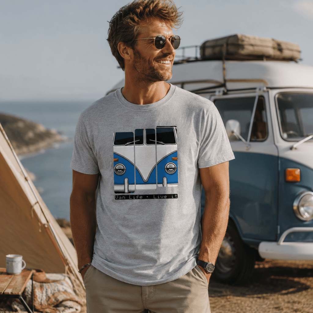 Man wearing a t-shirt with a van design, standing in front of a vintage van and tent by the sea.