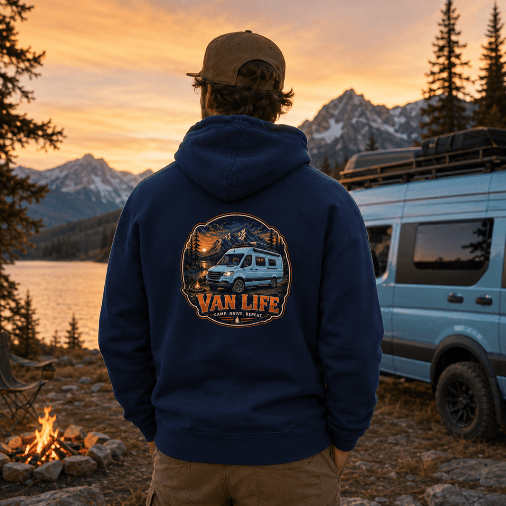 Person wearing a 'Van Life' hoodie with a sunset and van design, standing near a van and campfire.