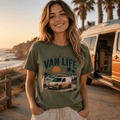 Woman wearing a 'Van Life' t-shirt by a van on a beach at sunset.