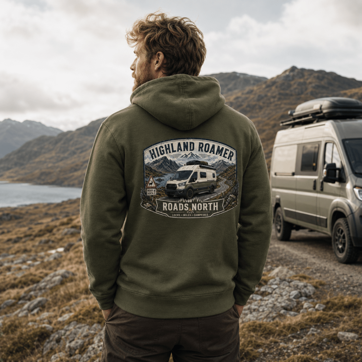 Man wearing a green hoodie with 'Highland Roamer' design, standing in a mountainous landscape with a van.