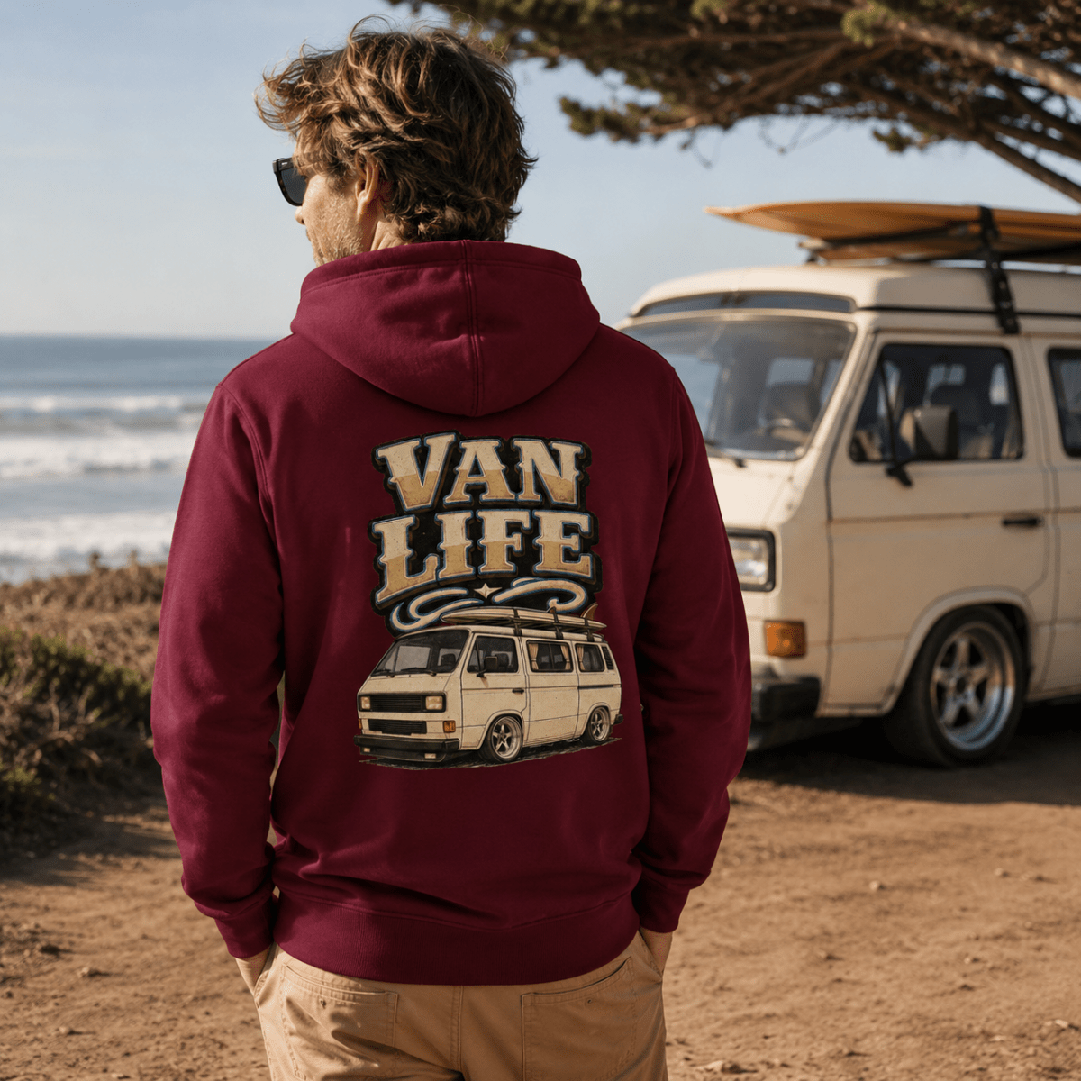 Person wearing a 'Van Life' hoodie by a van on a beach.