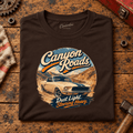 Canyon Roads Muscle Fastback American Drive Graphic T-Shirt — Dark Chocolate, folded front main hero on a worn automotive workbench – car-ts-0056