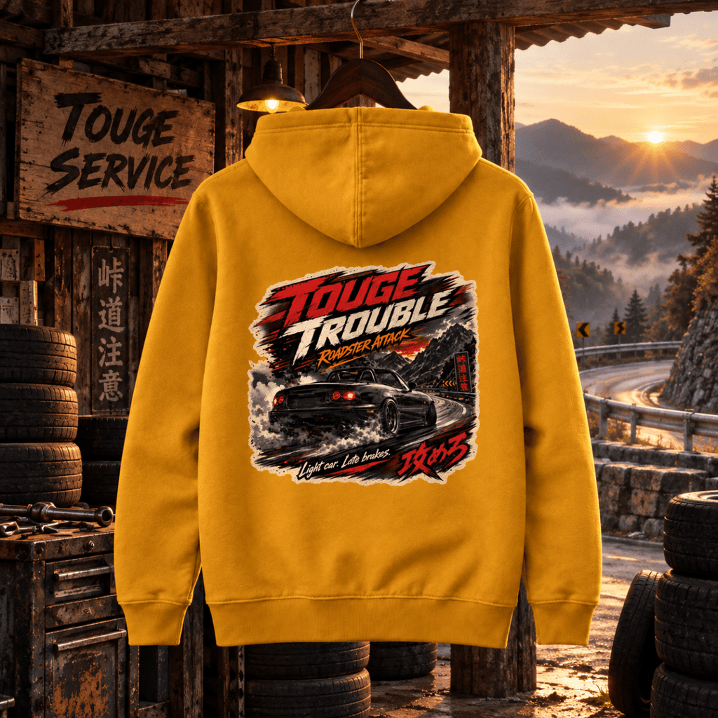 Touge Trouble mustard hoodie back in a gritty mountain-pass tyre shack