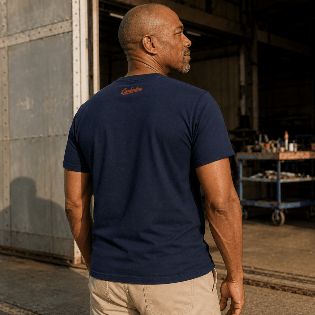 A man wearing a navy blue crewneck t-shirt with a small red embroidered 'Cruel Wolf' logo on the back, standing in a warehouse setting.