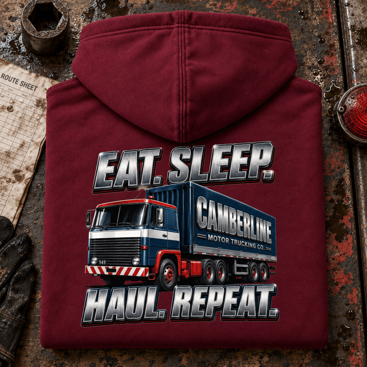 Burgundy Eat Sleep Haul Repeat lorry hoodie folded rear-up on a wet depot bench