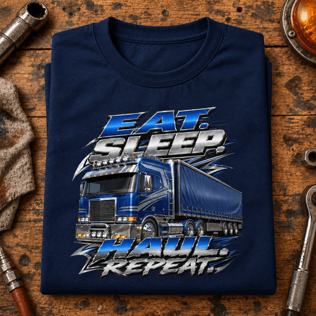 Navy chrome Eat Sleep Haul Repeat lorry T-shirt folded on a custom-truck workshop bench