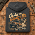 Folded dark grey Gear In Gravel Out Dust Is A Badge hoodie back on a workshop bench — car-hd-0003
