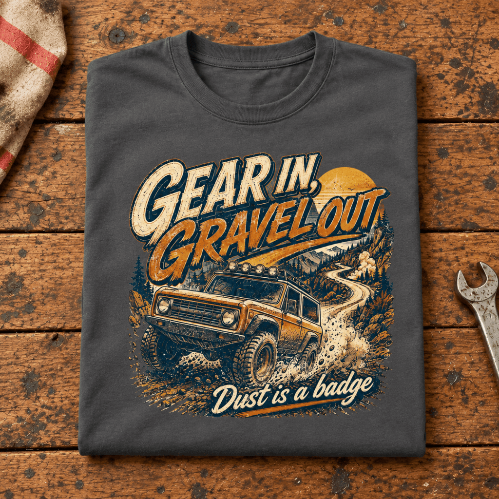 Folded dark grey Gear In Gravel Out Dust Is A Badge T-shirt front on a workshop bench — car-ts-0003