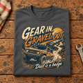 Folded dark grey Gear In Gravel Out Dust Is A Badge T-shirt front on a workshop bench — car-ts-0003