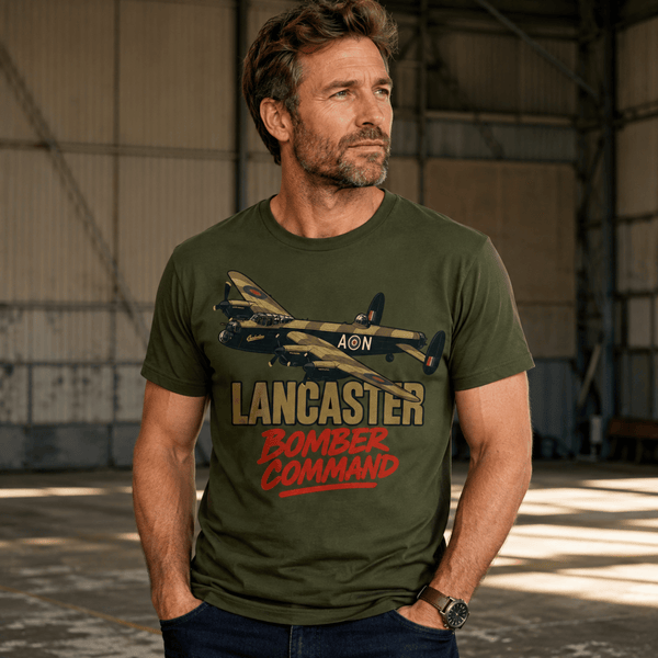A man wearing an olive green graphic t-shirt with a vintage Lancaster bomber design and the text 'LANCASTER BOMBER COMMAND', standing inside a large hangar.