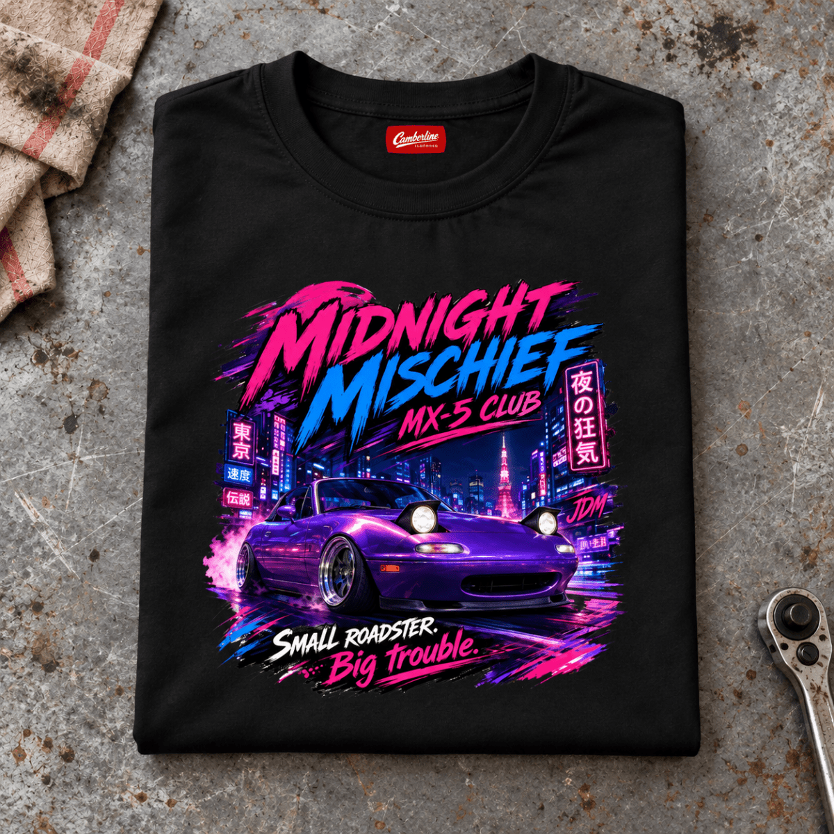 Folded black Midnight Mischief Club JDM Small Car Big Trouble T-shirt front on a workshop bench — car-ts-0048