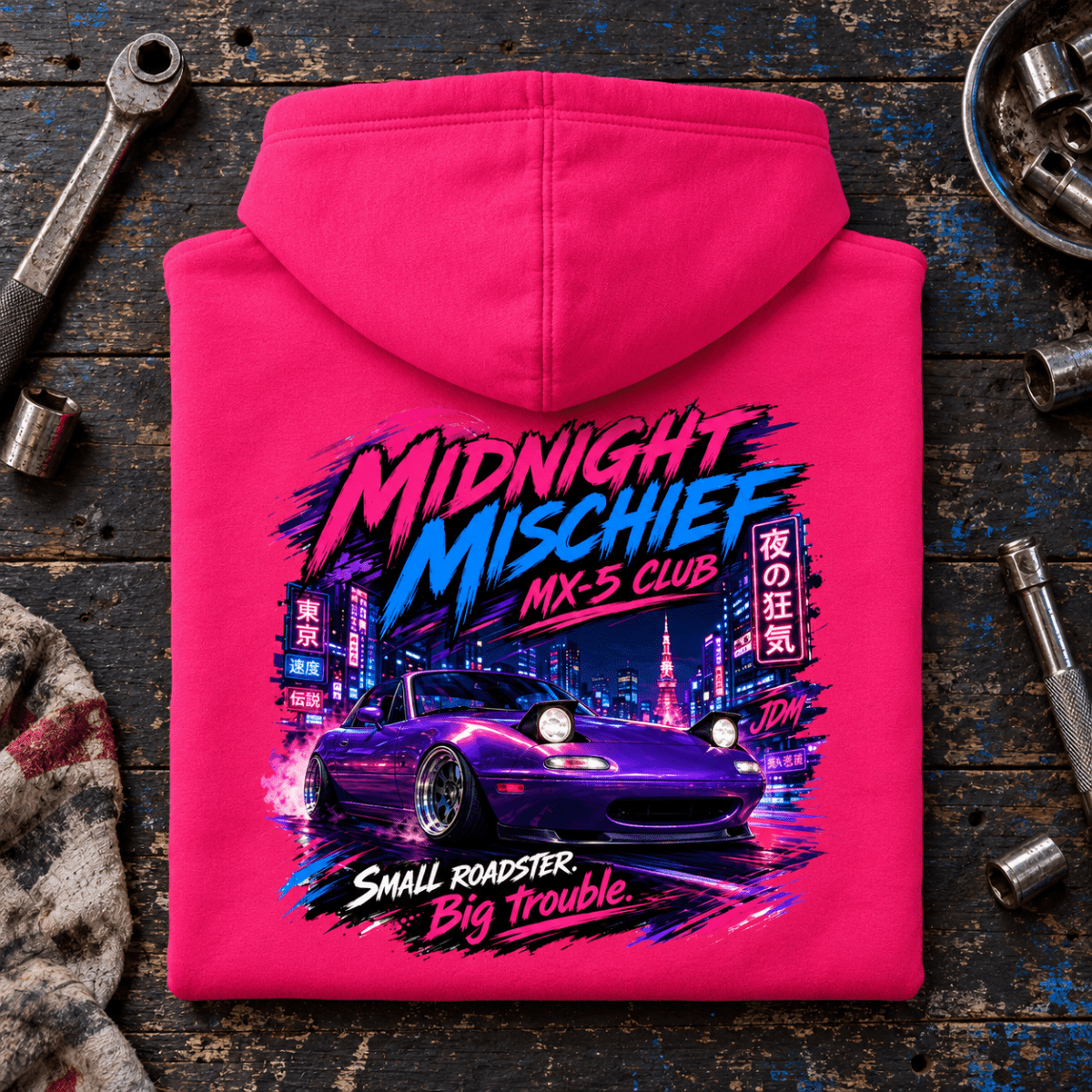 Folded hot pink Midnight Mischief roadster hoodie, rear print on a worn tuning bench — car-hd-0048