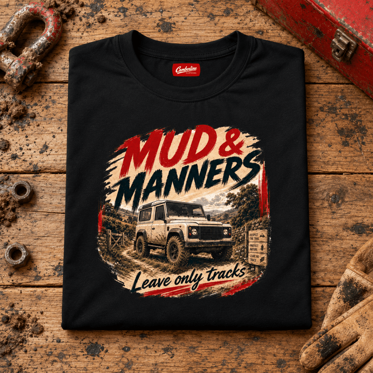 Camberline mud and manners 4x4 black T-shirt, folded front view on a workshop bench with the complete graphic visible.
