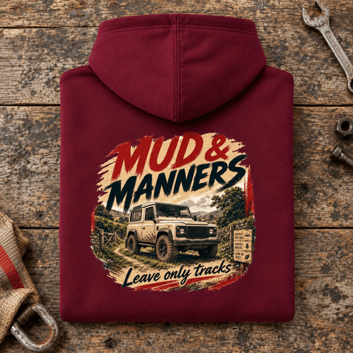 Camberline mud and manners 4x4 burgundy hoodie, folded rear view on a workshop bench with the complete graphic visible.