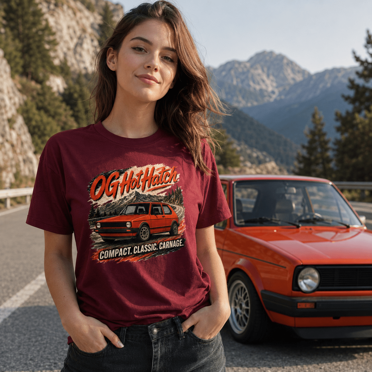 Woman wearing a maroon t-shirt with a graphic design of a red car, standing in front of a red car on a mountain road.
