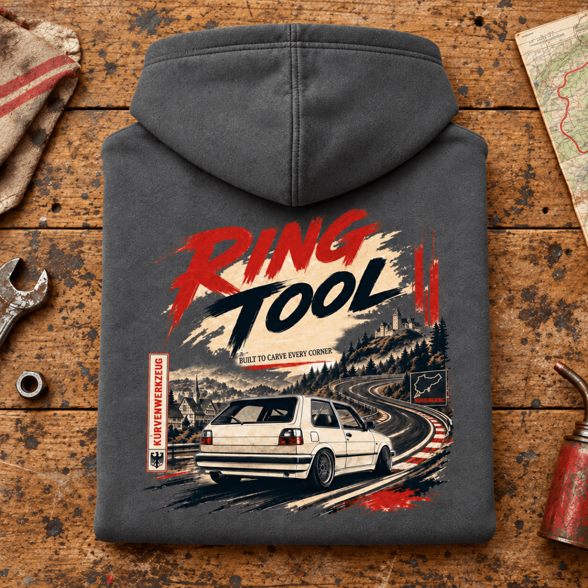 Hot Hatch Graphic Hoodie – Ring Tool Nürburgring Mk2 Track Day Line Art, folded back main hero on a worn automotive workbench – car-hd-0043
