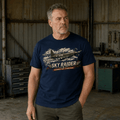A man wearing a navy blue graphic t-shirt with a vintage biplane design and the text 'SKY RAIDER' and 'EXCELLENT FLY, STRONG RACE' standing in a rustic workshop.