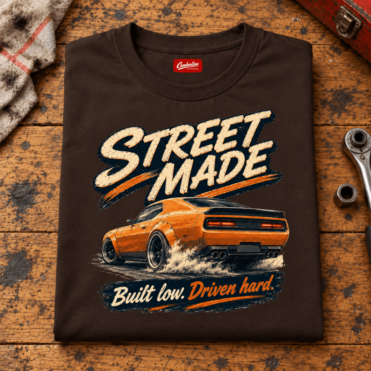 Folded dark chocolate Street Made Custom Build T-shirt front on a workshop bench — car-ts-0086