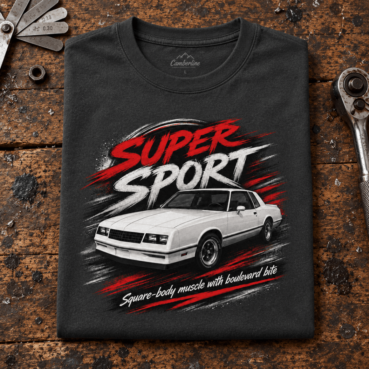 Super Sport Square-Body Muscle Coupe Graphic T-Shirt – Dark Grey, folded front hero on a worn automotive workbench – car-ts-0152