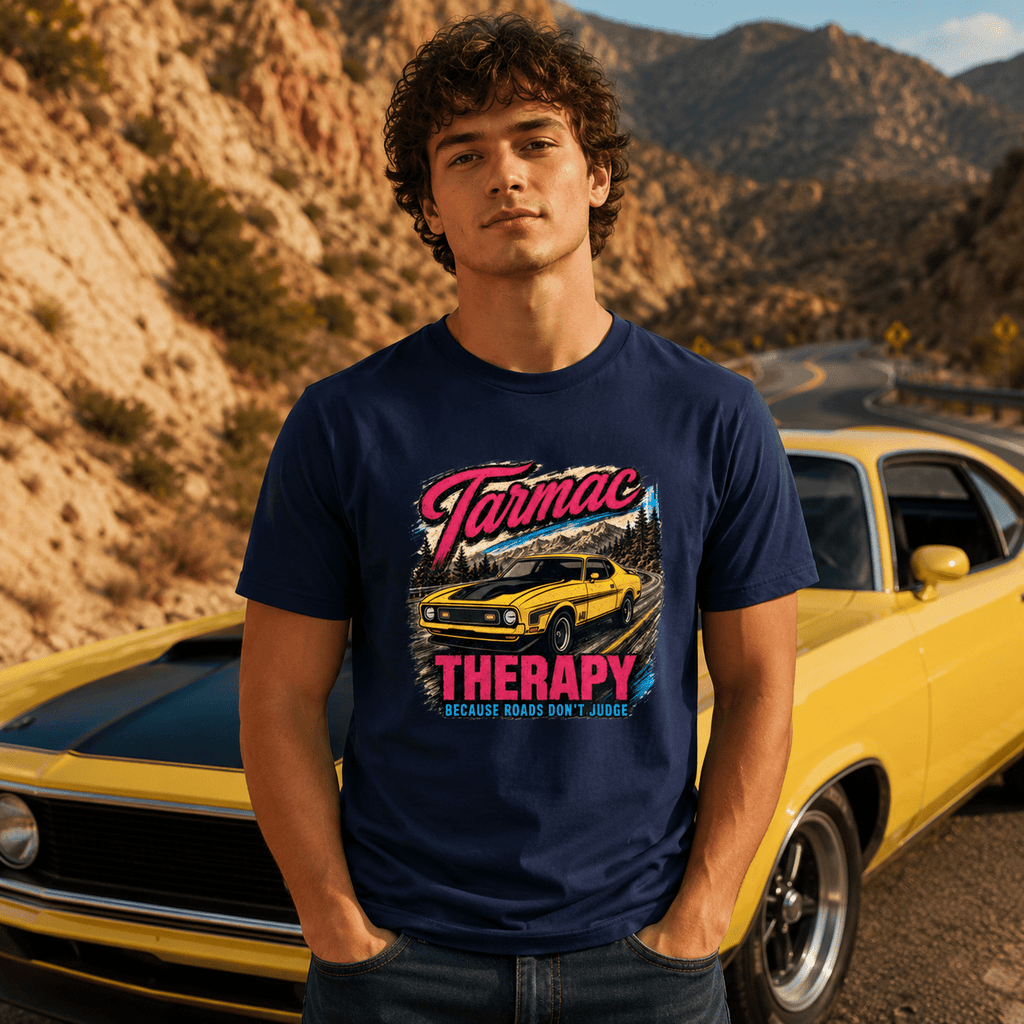 Man wearing a navy blue t-shirt with 'Tarmac Therapy' graphic in front of a yellow car on a mountain road.