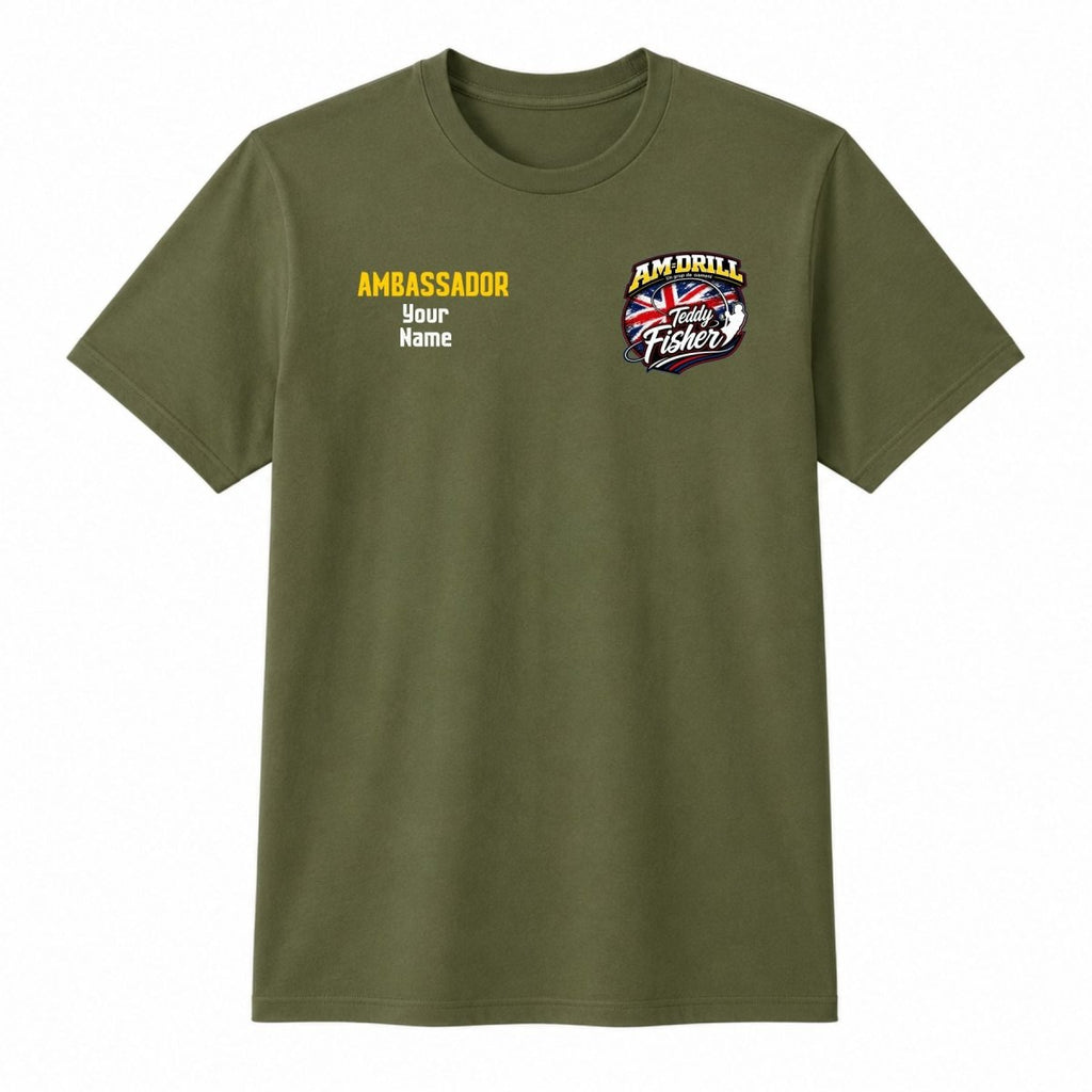An olive green short-sleeve t-shirt with custom graphic prints on the chest. The left chest features yellow and white placeholder text reading 'AMBASSADOR Your Name', and the right chest features a circular graphic with a Union Jack flag and the text 'AM DRILL Victory Fiddler'.