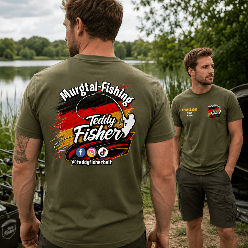 Two men outdoors by a lake wearing olive green t-shirts. The foreground man shows the back of the shirt with a large graphic reading 'Murgtal-Fishing' and 'Teddy Fisher' over a black, red, and yellow paint-splatter design.