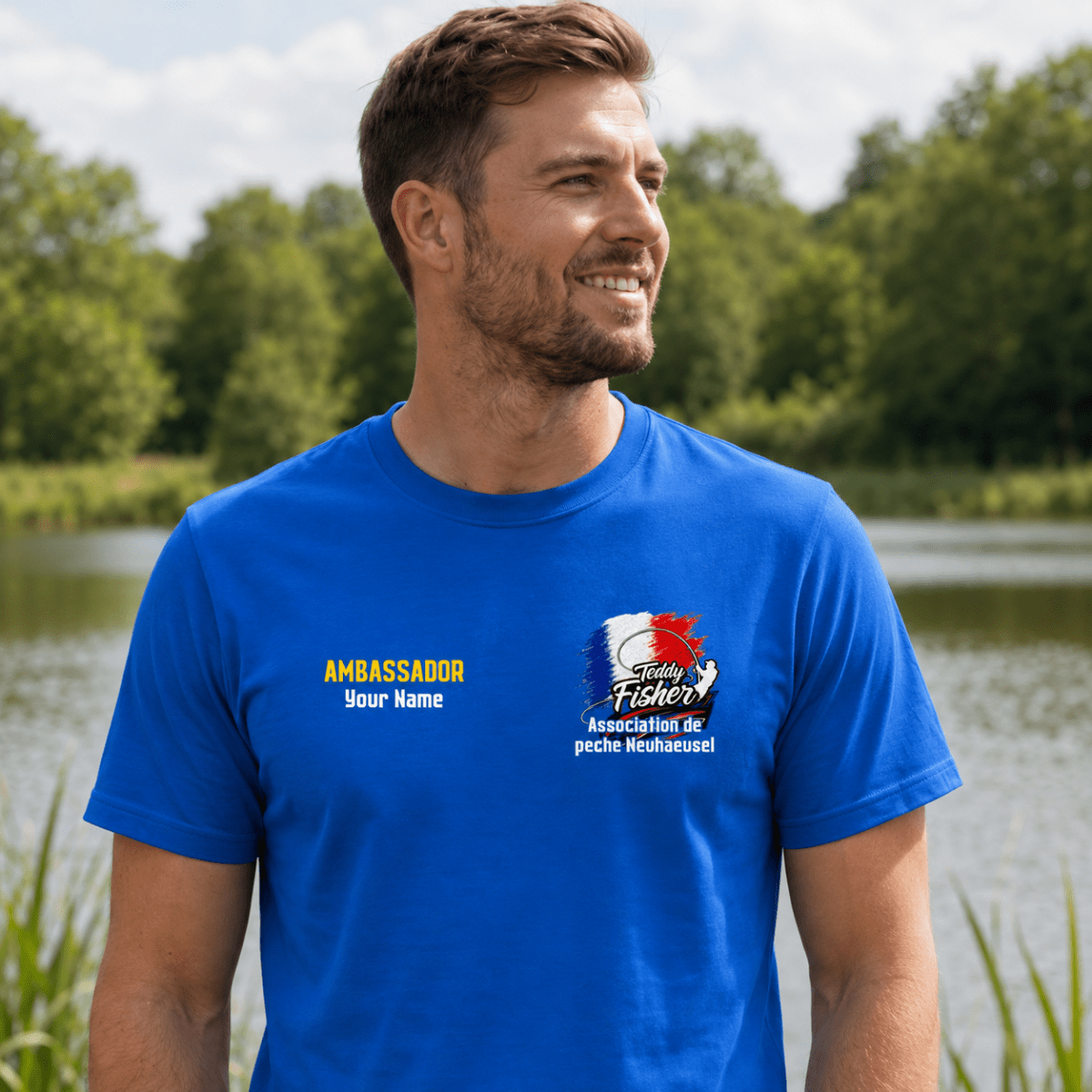 A man wearing a bright blue custom printed t-shirt with a fishing-themed graphic and text, standing outdoors in front of a lake and trees.