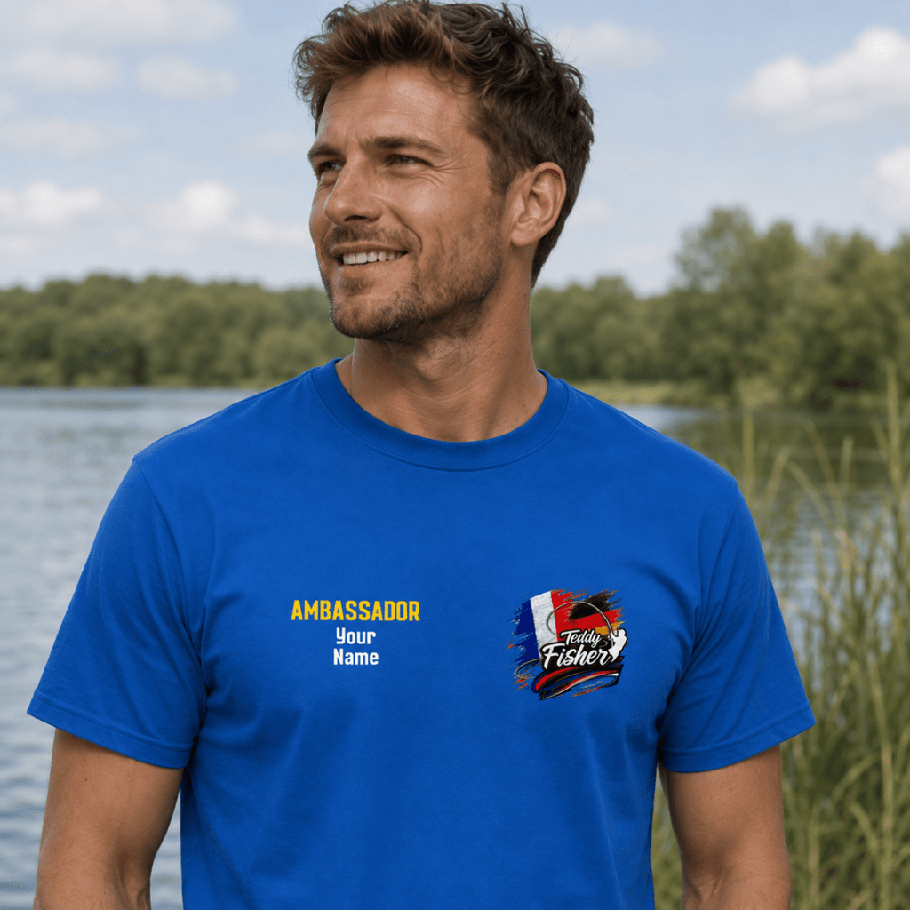 A man wearing a bright blue custom graphic t-shirt with 'AMBASSADOR Your Name' and a 'Texas Fishers' logo on the chest, standing outdoors near a lake.