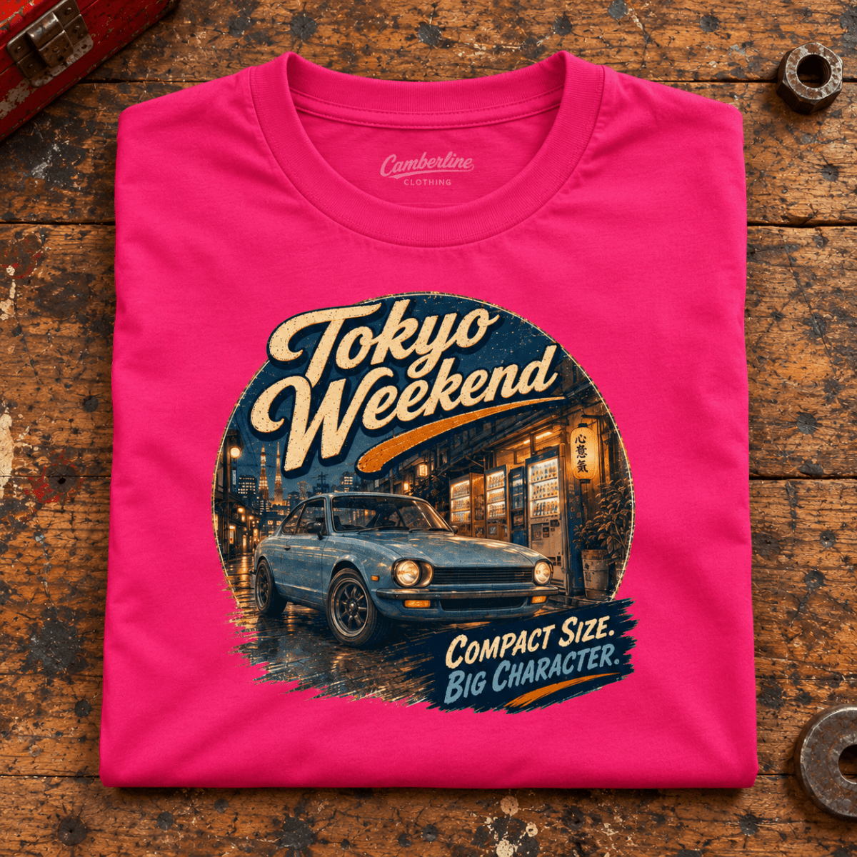 Tokyo Weekend Classic Compact JDM Street Car Graphic T-Shirt — Hot Pink, folded front main hero on a worn automotive workbench – car-ts-0057
