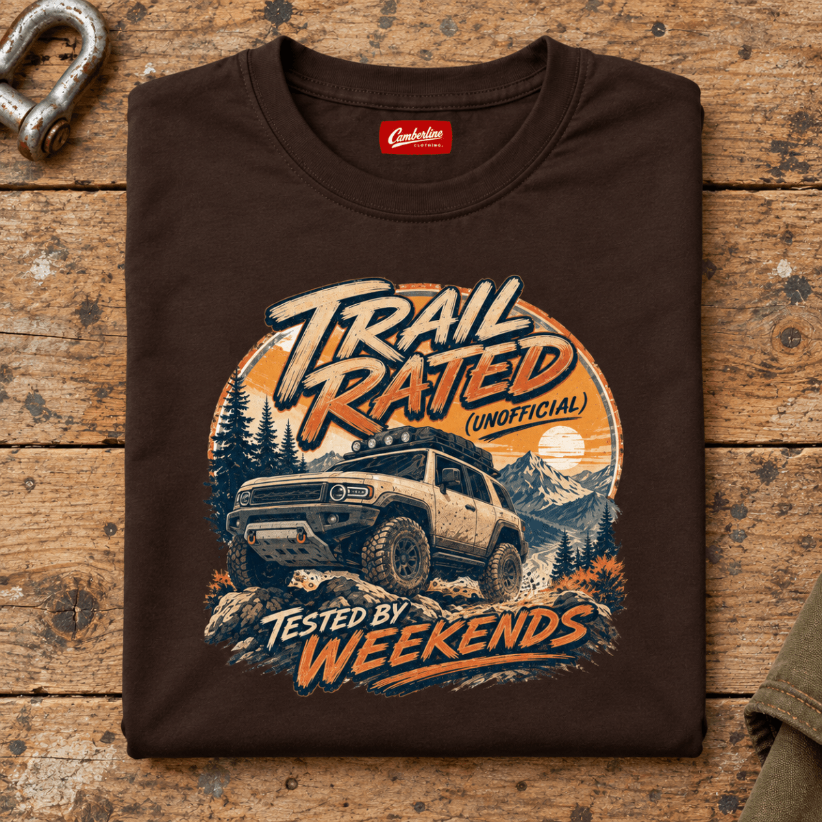 Folded dark chocolate Trail Rated Unofficial T-shirt front on a workshop bench — car-ts-0004