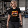 A woman wearing a black graphic t-shirt with a 'Trijet Titan' long haul sleeper train design, standing in a workshop environment.
